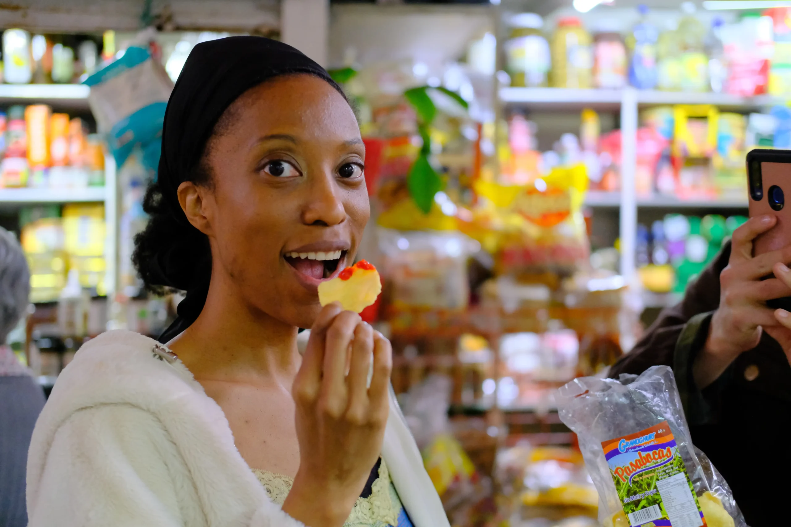 Woman enjoying tropical fruit during Bogota fruit tour, capturing the moment with her phone at a colorful market stall